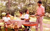 A vintage photo of a Black family sitting around a table and grilling outside