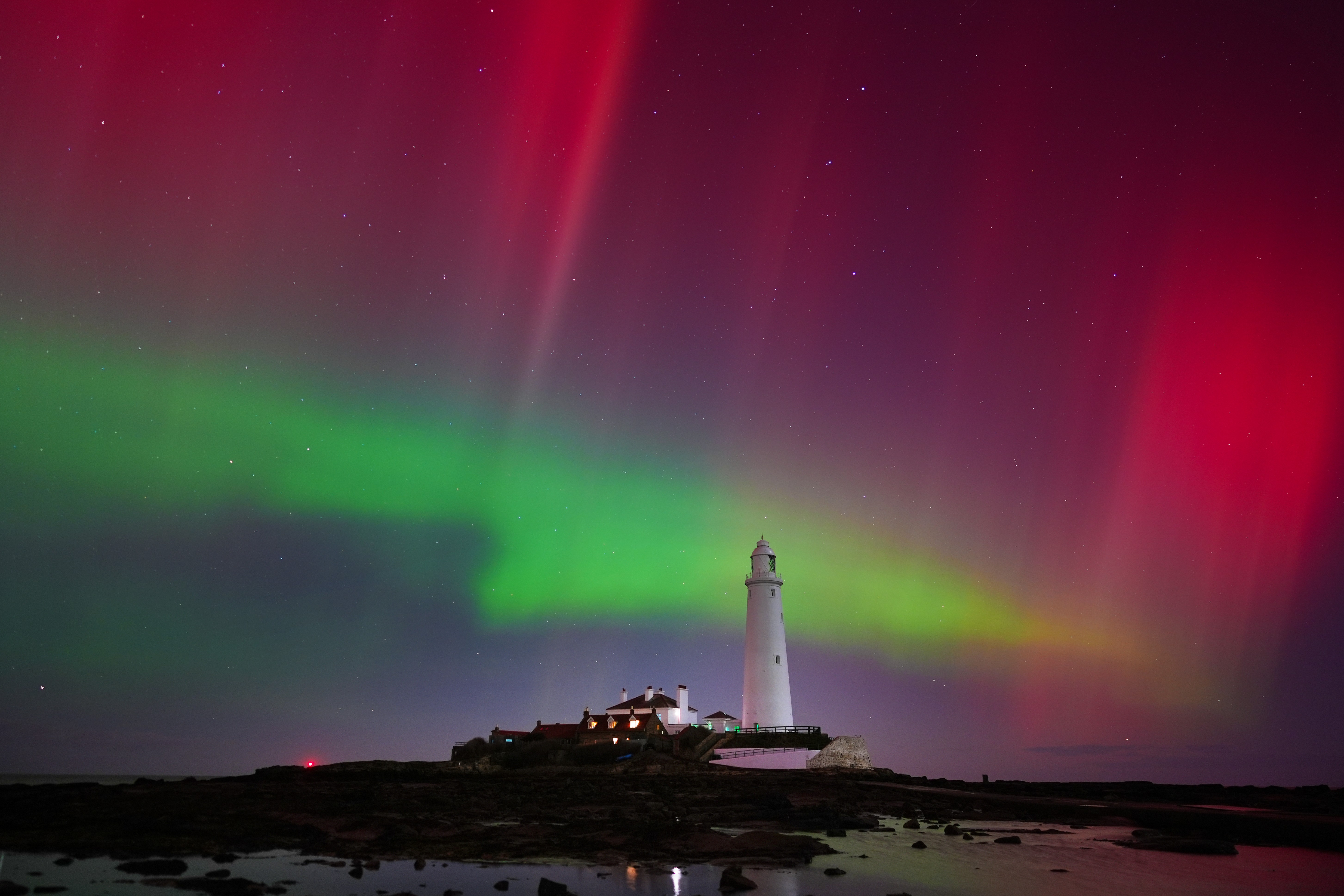 Green and red curtains of light, seen in the night sky above a light house