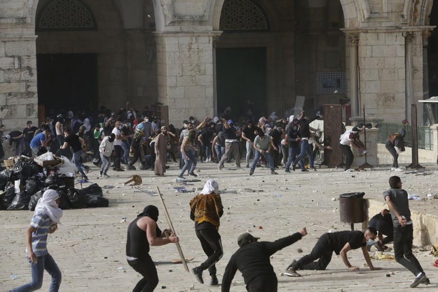 Protesters take cover and throw stones in a large compound.