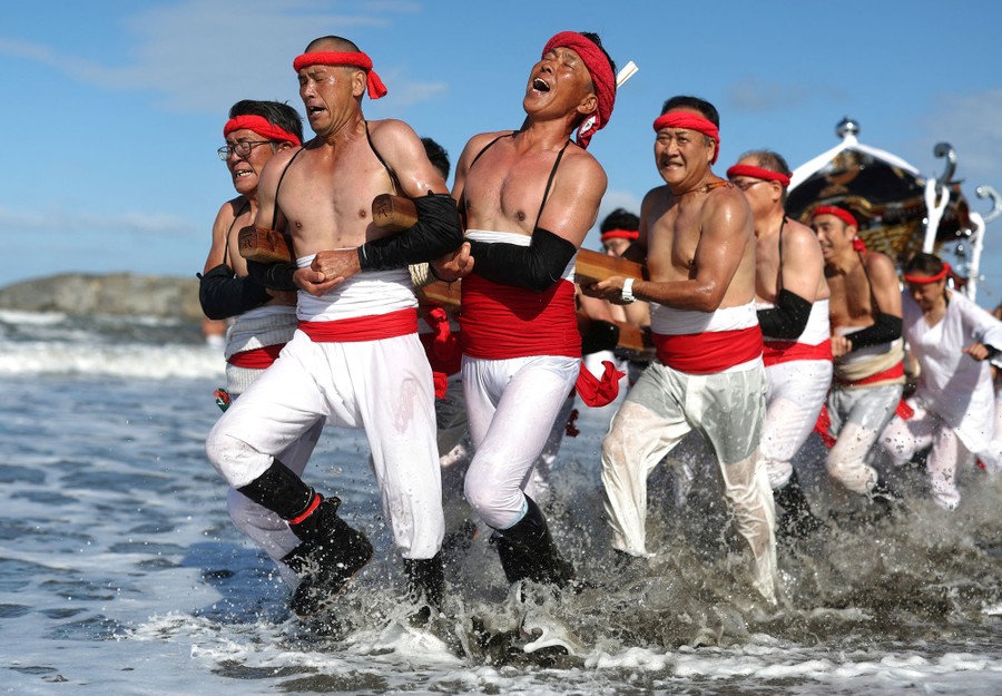 A group of people in traditional clothing carry a shrine into the surf.