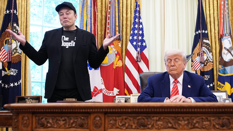 Elon Musk stands next to a seated Donald Trump.