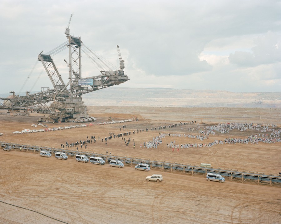 Hundreds of demonstrators gather in front of a long line of security and police officers beneath an enormous open-pit mining machine.