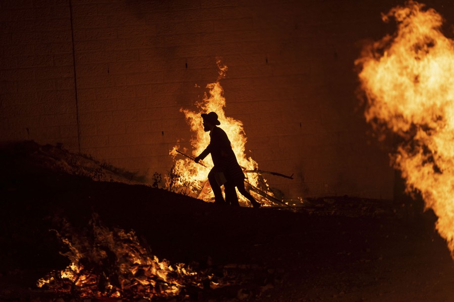 An ultra-Orthodox Jewish man walks amid several bonfires.