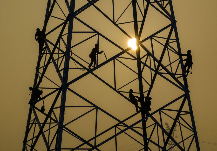 Six workers in silhouette, working in various positions high on a tall transmission tower