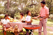 A vintage photo of a Black family sitting around a table and grilling outside