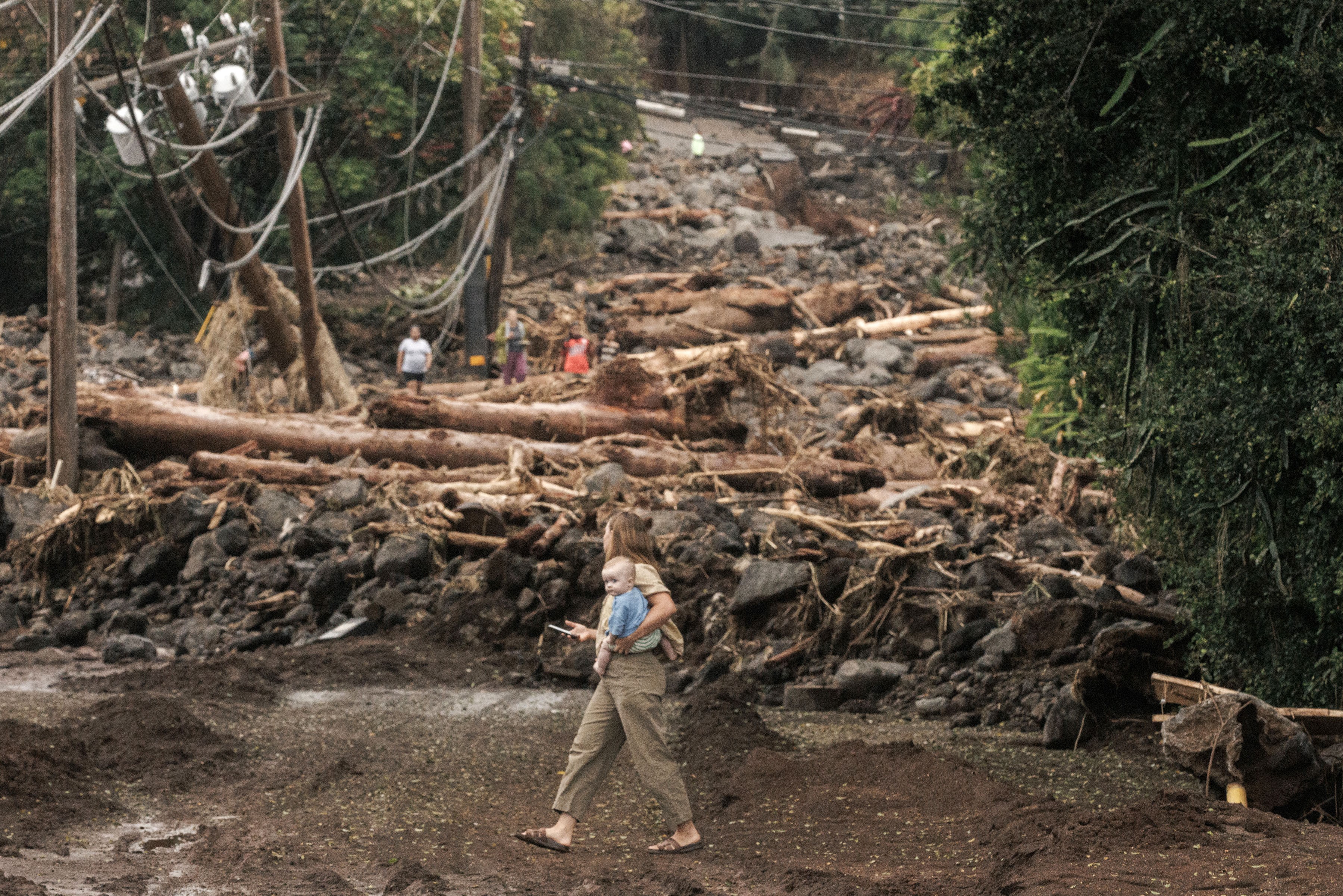 A woman and child walk past a debris-strewn street after a hurricane.