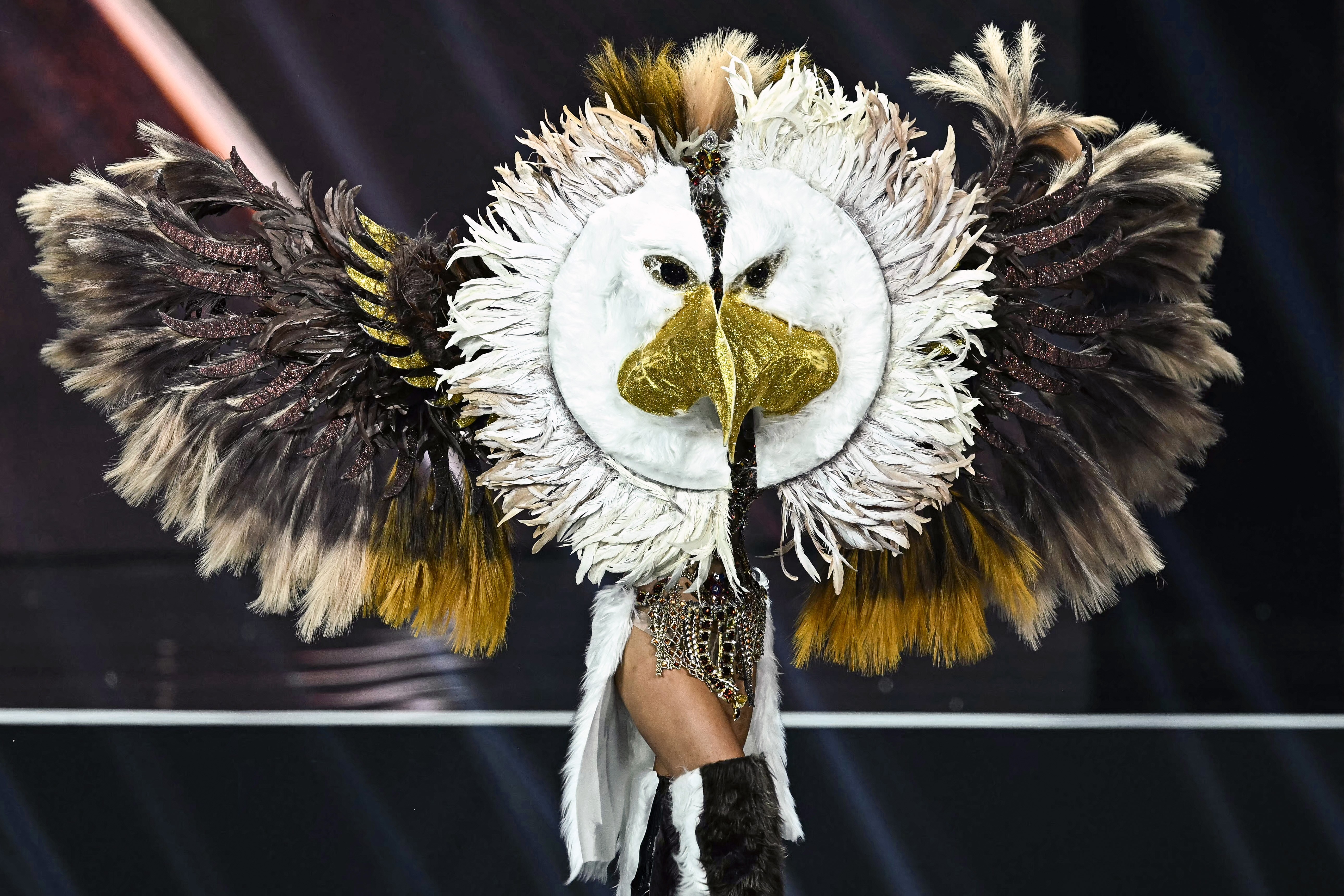 An entrant in the Miss Universe competition walks on stage wearing a large feathery eagle costume.
