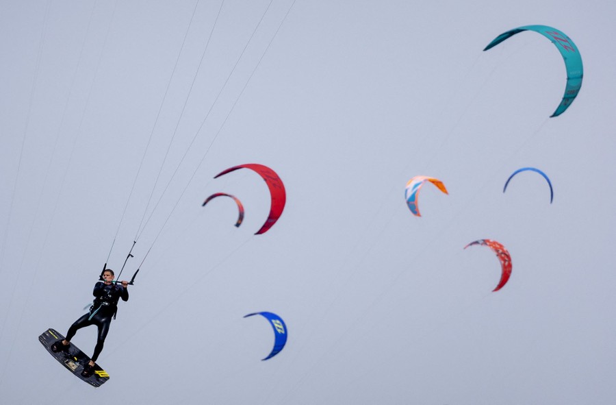 A kitesurfer hangs in the air in front of other kitesurfer sails.