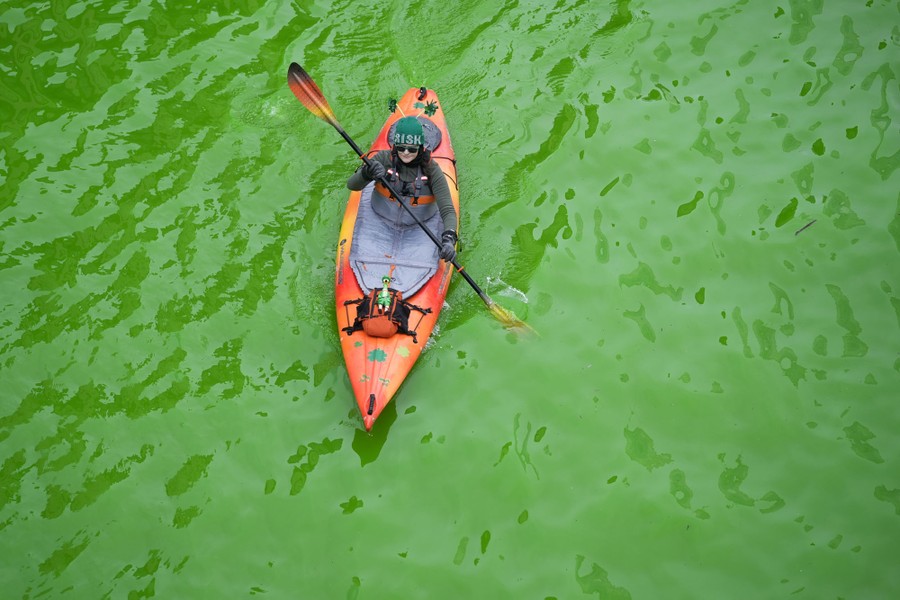 A kayaker floats on a river that has been dyed bright green.