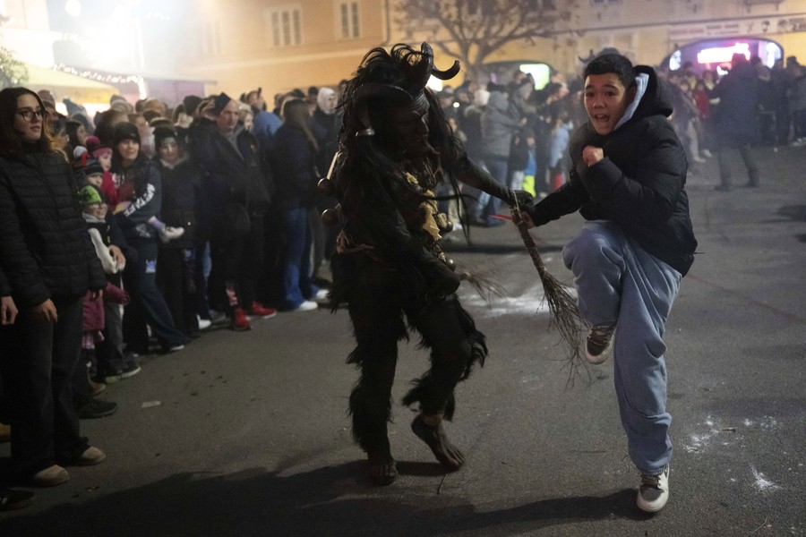 A performer wearing a traditional Krampus costume hits a young person with small sticks as they run.