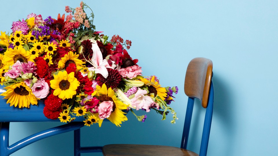 A profile view of a desk with flowers spilling off of it, against a blue background