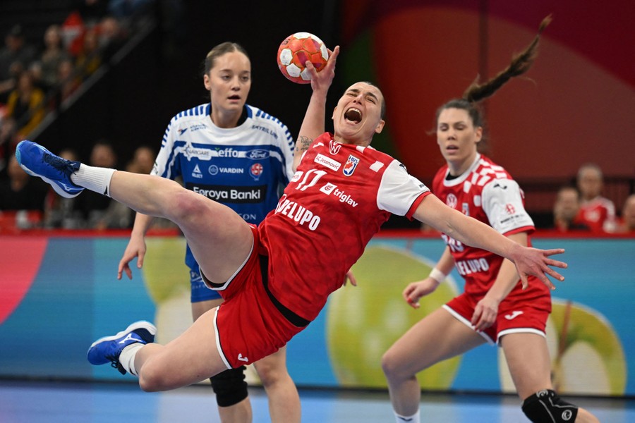A player makes a big leap and shouts while making a throw during a handball match.