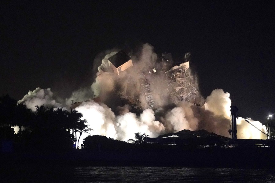 A night view of a collapsing building and surrounding cloud of debris