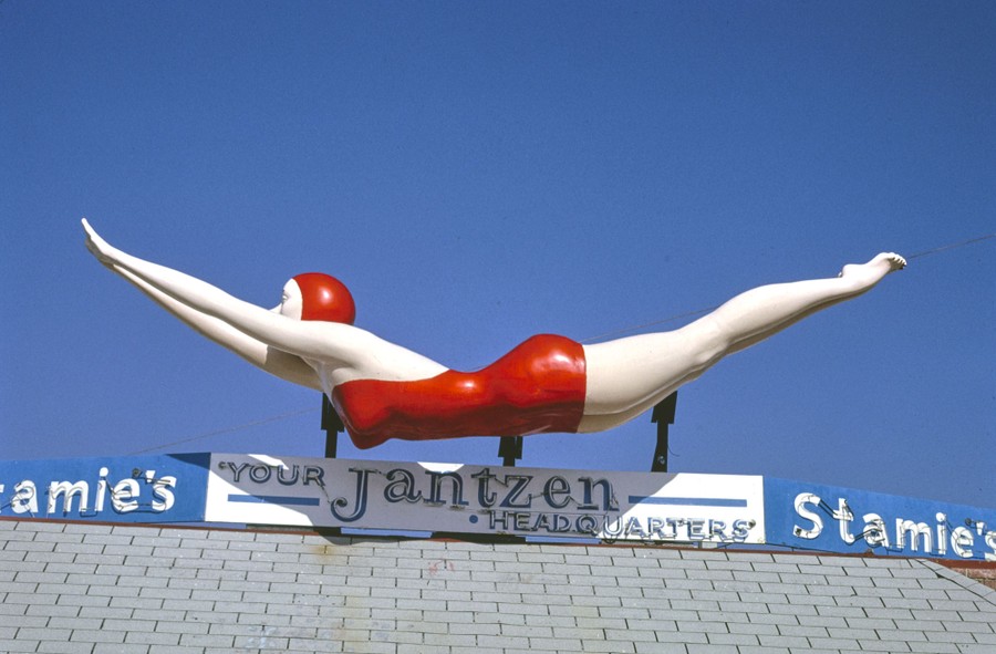 A 20-foot-long fiberglass woman diver in a red bathing suit is seen above a store.