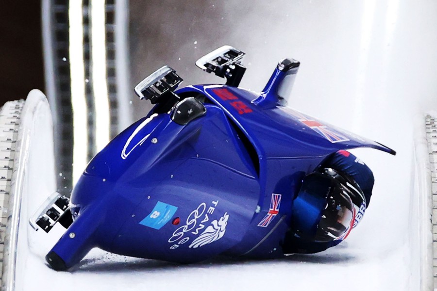 Two men in a bobsleigh slide upside-down, after a crash.