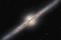 A spiral galaxy seen directly from the side, such that its disc looks like a narrow diagonal band across the image. A band of dark dust covers the disc in the center most of the way out to the ends, and the disc glows around that.