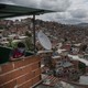 A person wearing a mask looks out over a view of the Petare slum in Caracas, Venezuela.