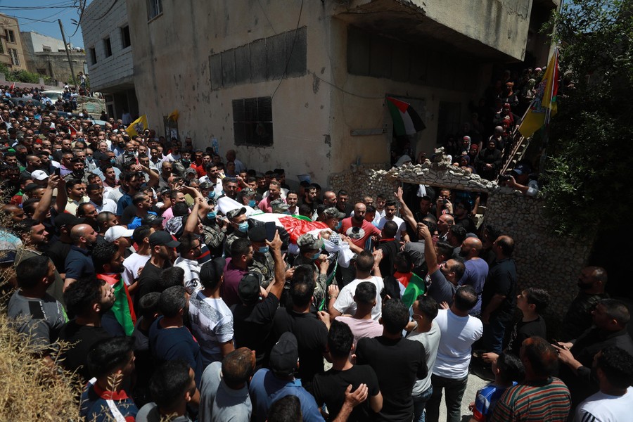 A large group of people help carry a body in a village street.