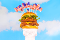 Double-decker chicken sandwich studded with American flags on a white pedestal