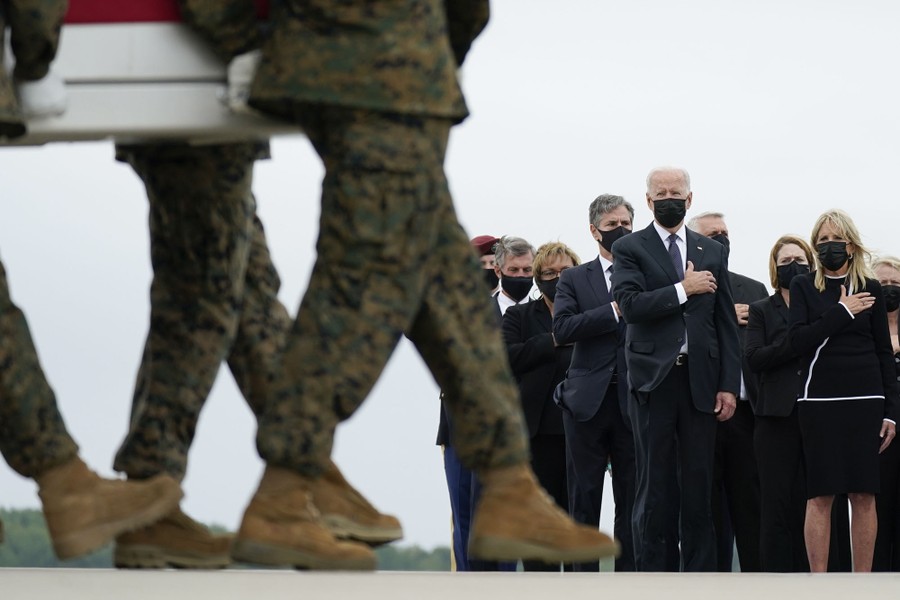 President Biden and others stand, hands over their hearts, watching as service members carry a casket off of a transport plane.