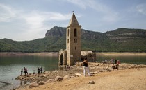 People walk around and look at the ruins of an old church standing in a reservoir with low water.