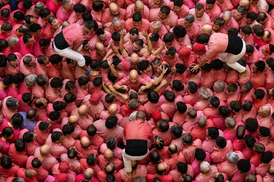 An elevated top-down view of a large crowd of people wearing red shirts, smashed tightly together, seen as three other people walk across their shoulders and heads
