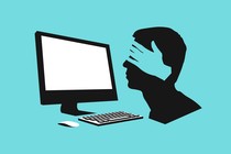 a silhouette of a face looking at a computer with hands covering its eyes against a light blue background