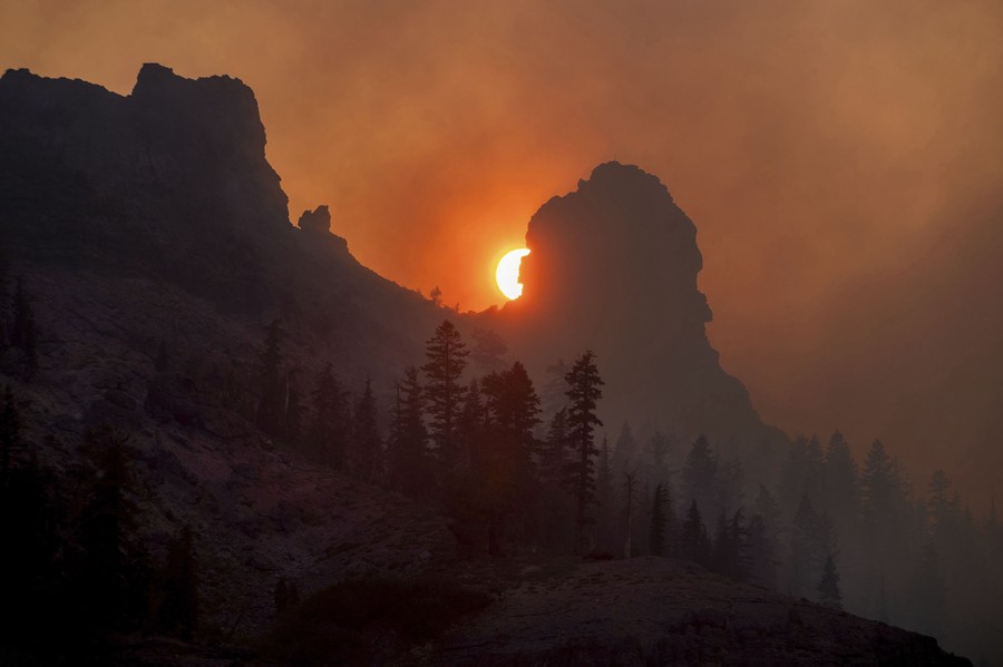 A low sun is seen behind a hilltop partially obscured by a smoky sky.