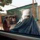 A woman in a burka puts her hand up to a car window, looking in at a passenger.