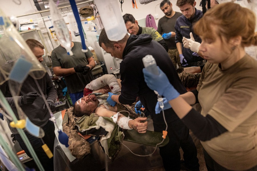 Army medics work on a wounded soldier who lies on a table.