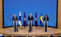 Three people stand at lecterns on a stage, with the flags of Finland, Ukraine, and NATO between them, during a press conference in Brussels.