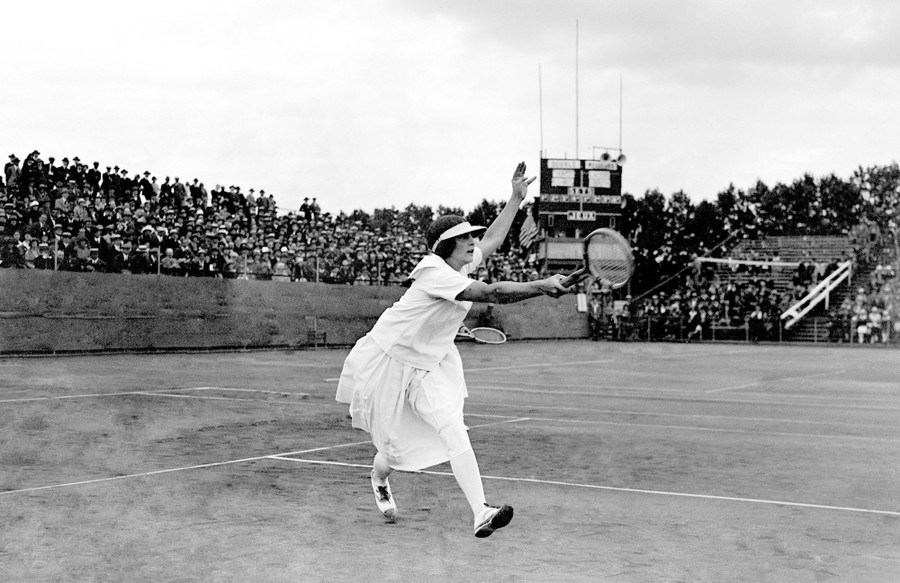 A tennis player runs while swinging her racket during a match.