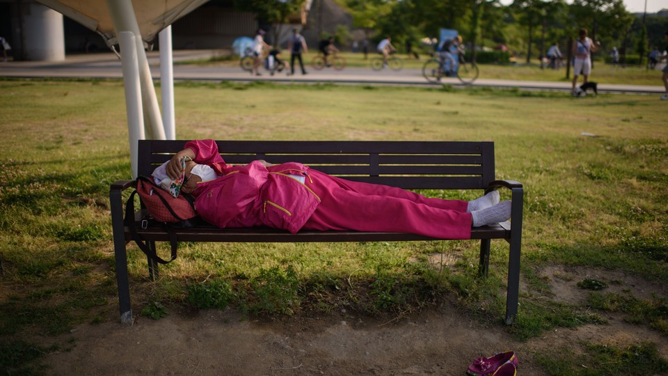 A woman wearing a face mask sleeps on a bench in Seoul.