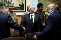 James Mattis stands in the center laughing and shaking hands with men in suits and military uniforms.