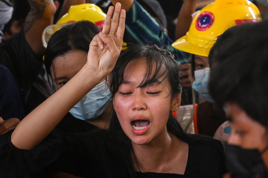A woman holds up three fingers in a salute, surrounded by supporters.