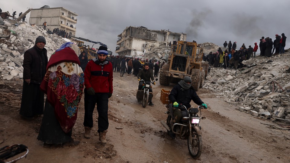 Photo showing Syrian civilians inspecting a destroyed residential building following a 7.8-magnitude earthquake