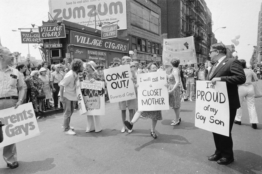 People march in a gay-pride parade, carrying signs that say, for instances, "I will not be a closet mother" and "I'm proud of my gay son."