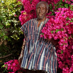 The author Ngũgĩ wa Thiong'o standing in front of pink flowers in an African-made shirt