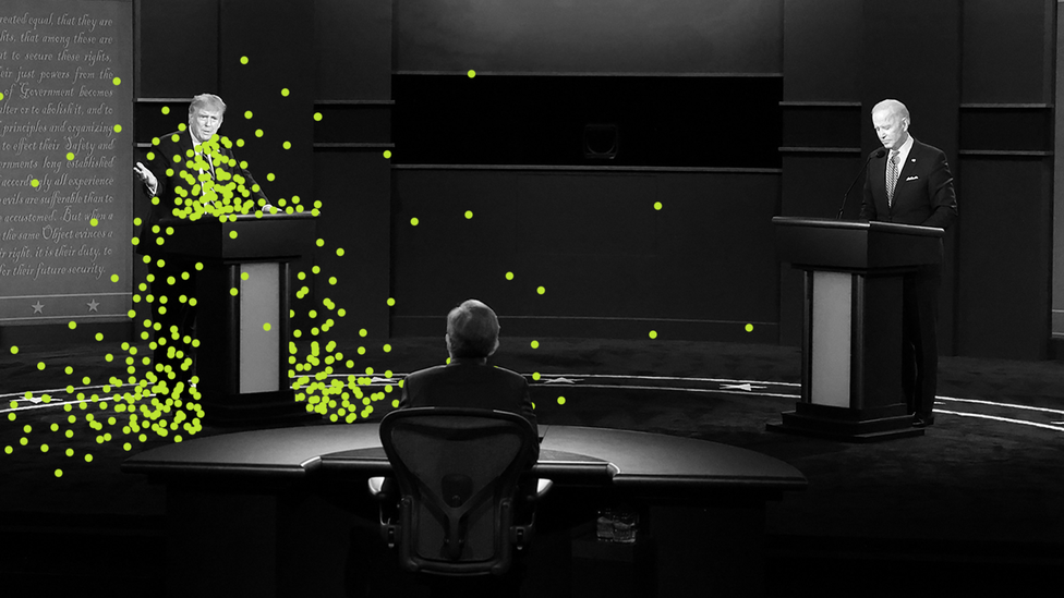 Donald Trump stands at a podium across from Joe Biden, surrounded by green virus particles