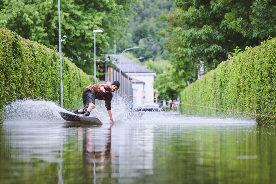 A person rides a wakeboard through a flooded street.
