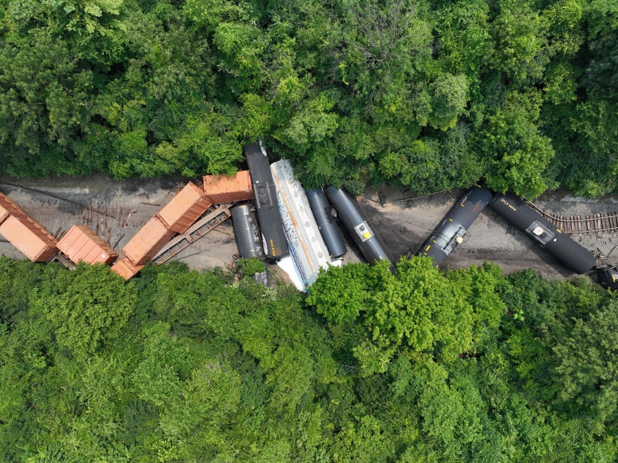 An aerial view of a derailed freight train amid a stand of trees