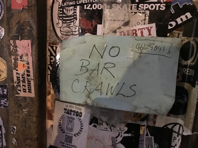 A dirty paper sign on the door of a bar, reading "NO BAR CRAWLS."