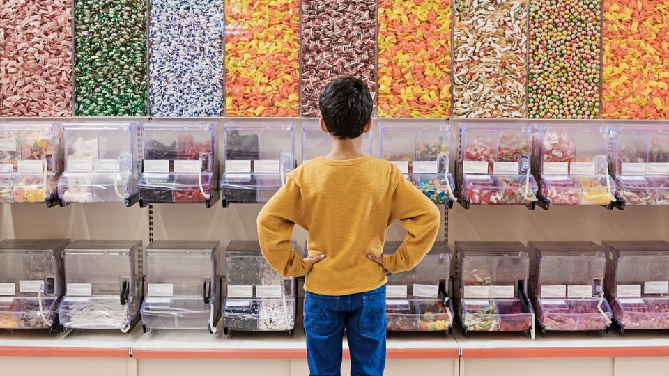 A young boy faces a wall of candy dispensers.