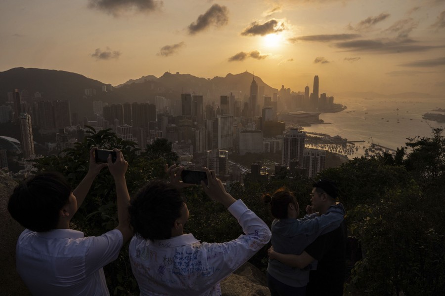 People take pictures of a sunset above the harbor and skyline of Hong Kong.