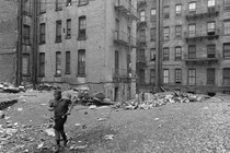 A black-and-white photo of a child running through New York City tenements