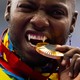 An athlete playfully bites a gold medal during a ceremony. Their canine teeth have been modified to look like long fangs.