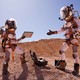 Two 'Stars on Mars' contestants, dressed in orange-and-white spacesuits, interact in the Mars-esque Australian desert