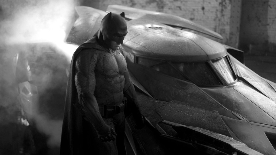 Black-and-white photo of Ben Affleck playing Batman, standing next to the Batmobile