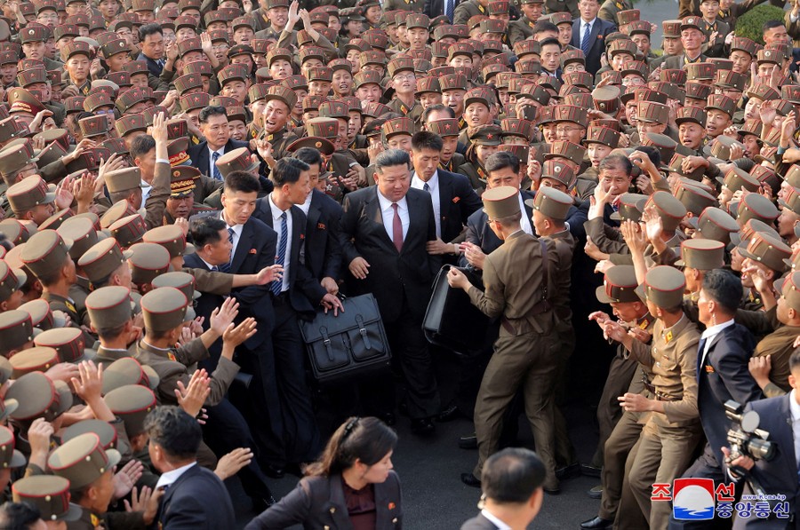 Dozens of young men in military uniforms clamor around North Korean leader Kim Jong Un.