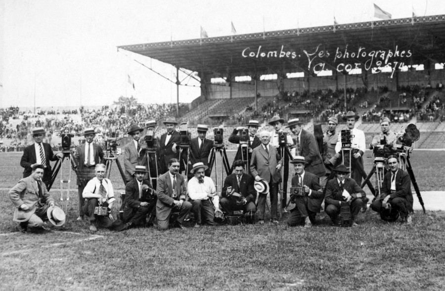 A group photo of a couple of dozen photographers in 1924, seen inside a sports stadium.